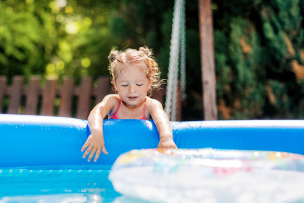 A charming baby touches the water in an inflatable pool in the garden and smiles - Foto, immagini