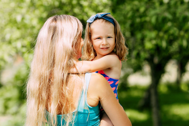 Una giovane madre tiene la sua figlioletta tra le braccia in una giornata estiva in giardino o al parco - Foto, immagini