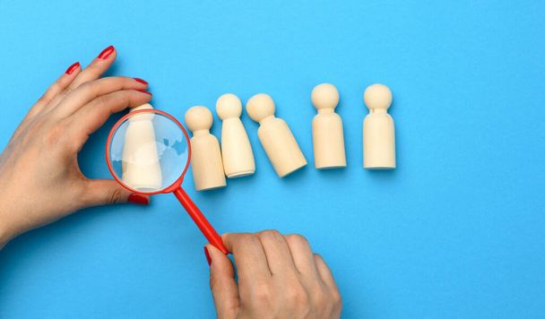 wooden figures of men on a blue background and a red magnifying glass. Recruitment concept, search for talented and capable employees, career growth - Photo, Image