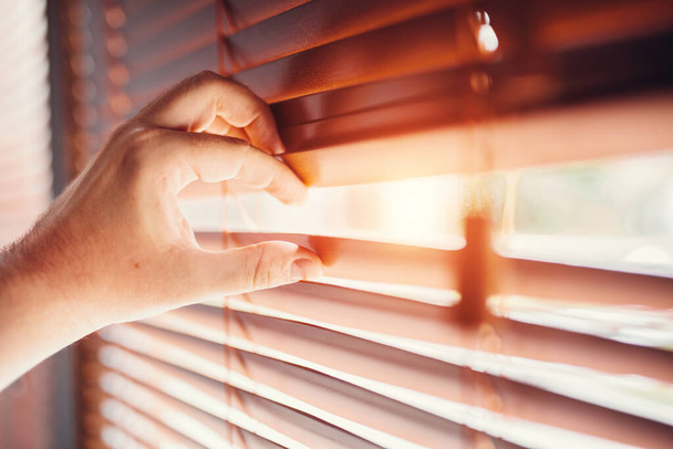 Peeping through window blinds. Hand opening shutters - Foto, Imagen
