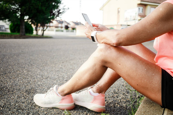 Brunette legs of hispanic woman with sportswear sat down on an asphalt road - Photo, image