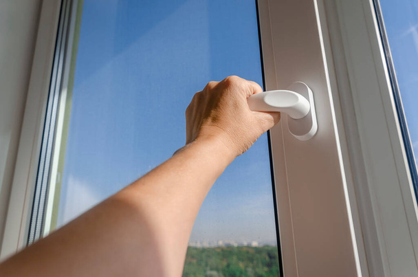 Dłoń kobiety otwiera uchwyt plastikowego okna przed błękitnym niebem - Zdjęcie, obraz