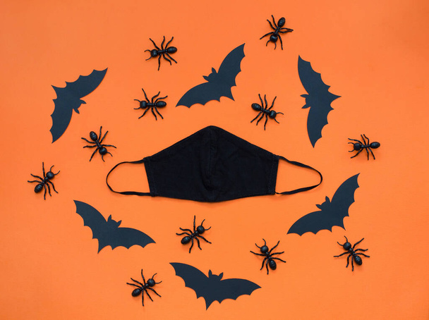 Fekete arc maszk és Halloween minta fekete díszítéssel narancssárga alapon. Fekete papírdenevér, hangyák és szemek, Halloween party dekorációk a világjárvány Coronavirus - Fotó, kép