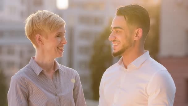 Çok ırklı iş arkadaşı çift Arap kökenli İspanyol erkek ve yetişkin beyaz kadın güneş ışığında dışarıda durmuş sohbet görüşmeleri kameraya bakıp gülümsüyor ve başlarını sallıyorlar. - Video, Çekim