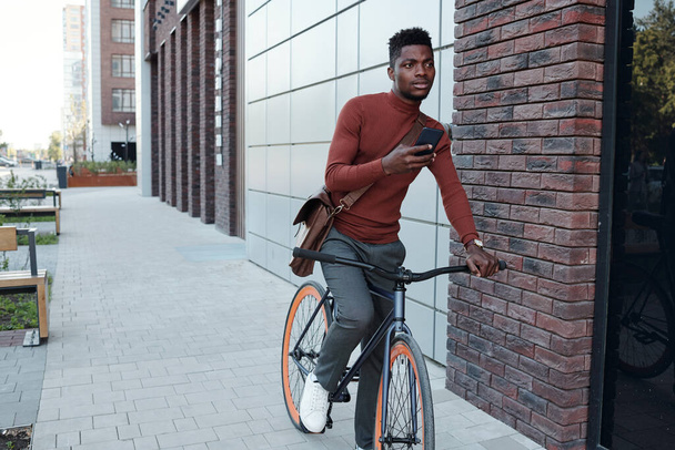 Молодой бизнесмен пользуется смартфоном во время езды на велосипеде - Фото, изображение