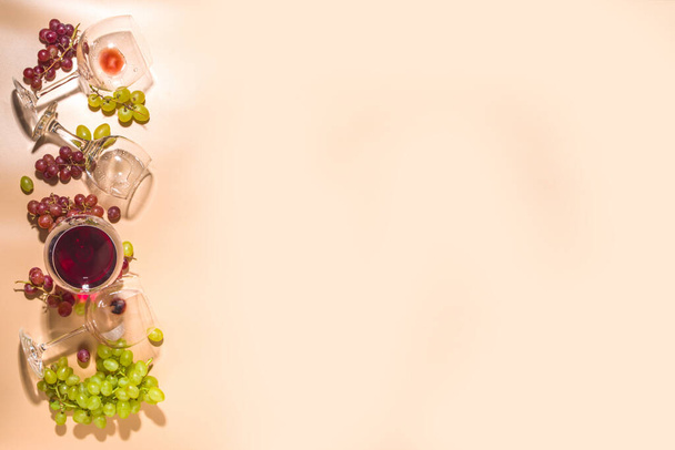 Vasos de vino tinto y blanco con sol y sombras, con botella y decantador, racimo de uvas, sobre fondo de color cremoso, vista superior aplanada Degustación de vinos, cosecha de otoño, concepto de bodega  - Foto, Imagen