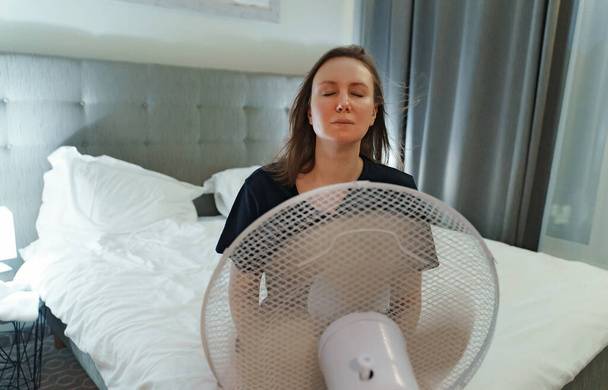 Mujer trata de refrescarse durante el intenso calor en frente de ventilador de enfriamiento. - Foto, imagen