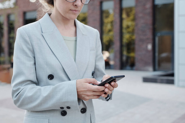 Молодая предпринимательница прокручивает в смартфоне по городской среде - Фото, изображение