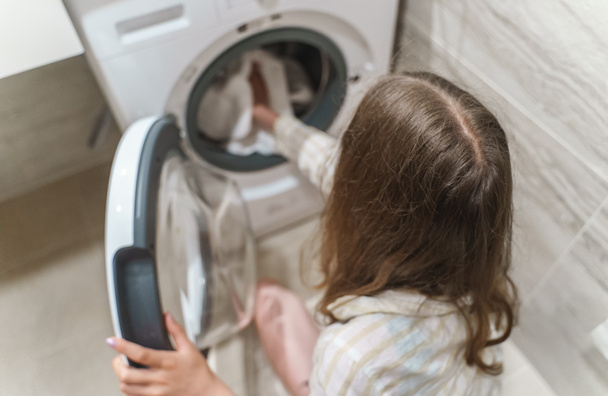 Teenage girl loading clothes into washing machine. - Foto, Imagem