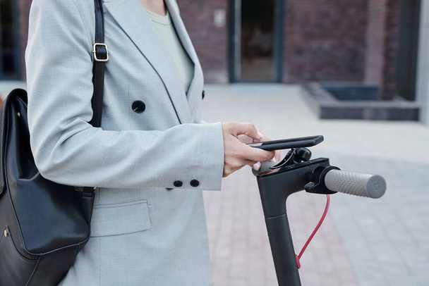Zakenvrouw met smartphone met behulp van mobiele applicatie te huur scooter - Foto, afbeelding