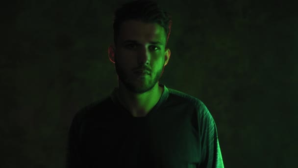 Neon ışıklı karanlık bir odada elleri göğsünde katlanmış vahşi sakallı genç bir sporcunun portresi. 4K - Video, Çekim