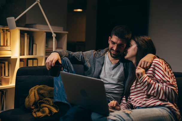 couple using laptop computer , while sitting on sofa at home , evening mood - 写真・画像