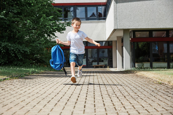 Happy boy running from school at the end of the school day with a backpack in hand. The beginning of the vacation. - Фото, изображение