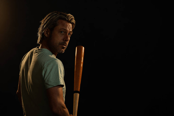 Hombre rubio en una camiseta verde claro se para con un bate de béisbol. - Foto, imagen