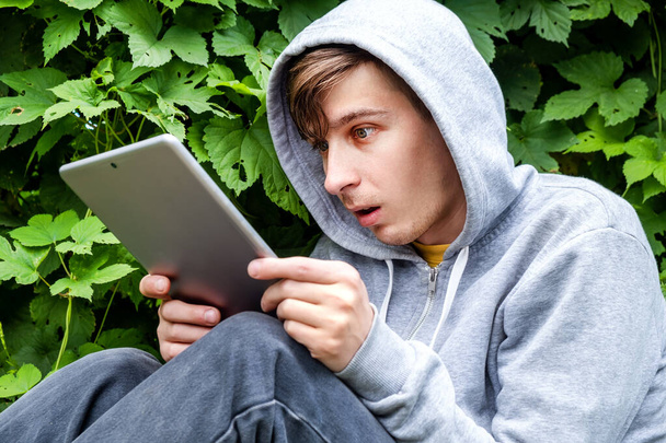 Surprised Young Man with a Tablet Computer on the Green Leaves Background outdoor - Foto, immagini
