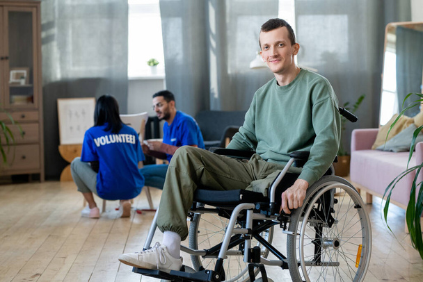 Young disabled man sitting in wheelchair against volunteers - Фото, зображення
