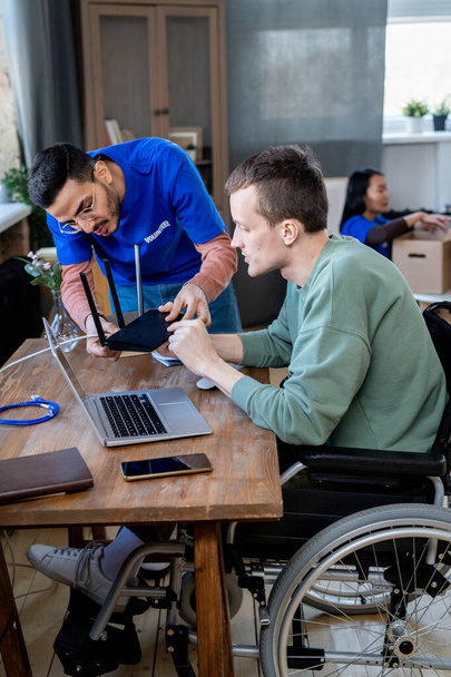 Volontario maschile che aiuta l'uomo disabile con router - Foto, immagini