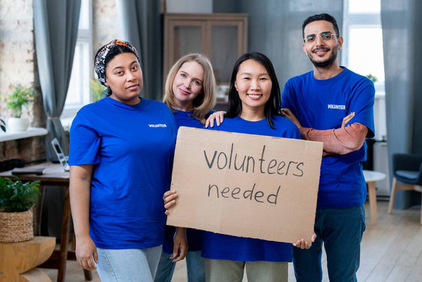 Vier jonge multiraciale vrijwilligers in blauwe t-shirts - Foto, afbeelding