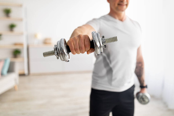 Active, sports at home, wellness and healthy lifestyle. Athletic middle-aged male lifting dumbbells in living room, crop - Foto, afbeelding