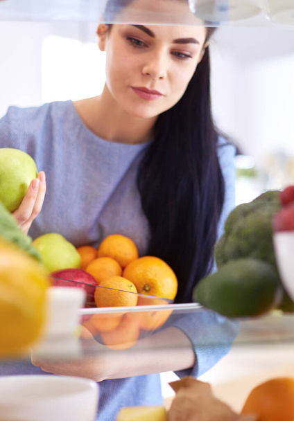 Smiling woman taking a fresh fruit out of the fridge, healthy food concept - Zdjęcie, obraz