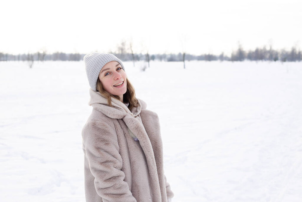 Chica joven en ropa beige, abrigo de piel hecha de paseos de piel artificial en invierno - Foto, Imagen