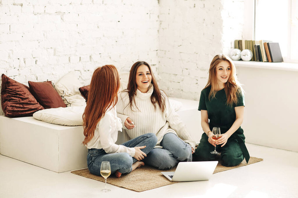 Full body νεαρές γυναίκες που κάθονται στον πάγκο και περιηγούνται στα μέσα κοινωνικής δικτύωσης στο laptop ενώ ξεκουράζονται στο light room στο σπίτι - Φωτογραφία, εικόνα
