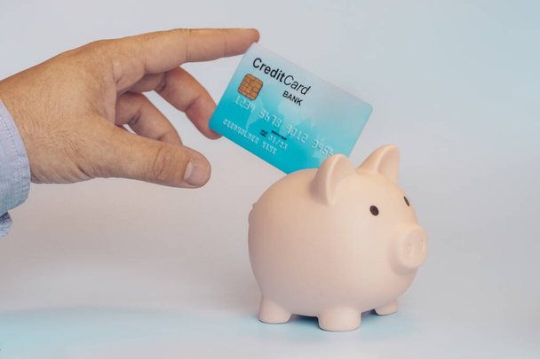 Mann steckt Kreditkarte in Sparschwein Das Konzept des Sparens mit der EC-Karte. - Foto, Bild