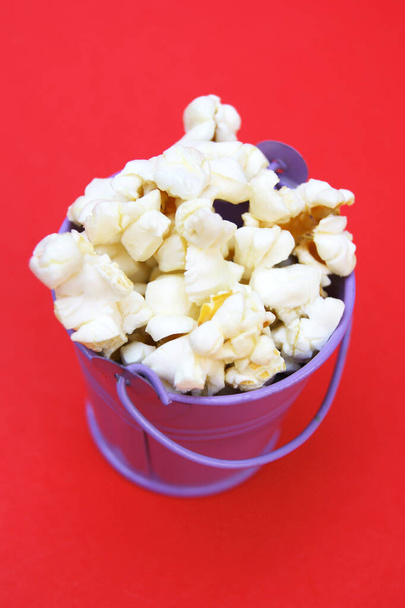 Frisches Popcorn in einem kleinen dekorativen eisernen Eimer auf rotem Hintergrund. - Foto, Bild
