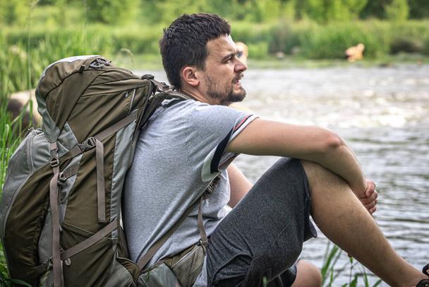 Un turista con una gran mochila se sentó a descansar cerca del río. - Foto, imagen