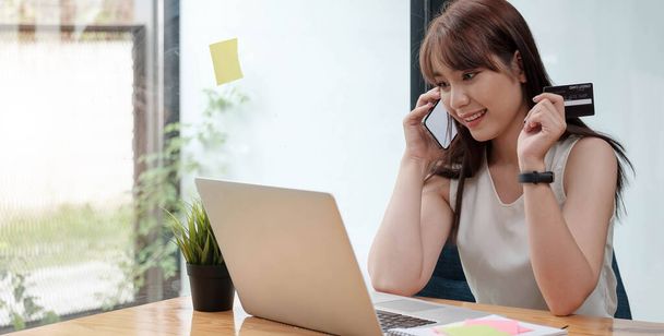 Mujer sonriente sentada en la oficina hablando por teléfono móvil y pagando en línea con tarjeta de crédito en tableta. - Foto, imagen