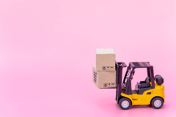 Logistics, and delivery service - Forklift μοντέλο και χάρτινα κουτιά ή δέμα με λογότυπο καλάθι αγορών σε ροζ φόντο. Υπηρεσία αγορών στο διαδίκτυο και προσφέρει παράδοση κατ 'οίκον. - Φωτογραφία, εικόνα