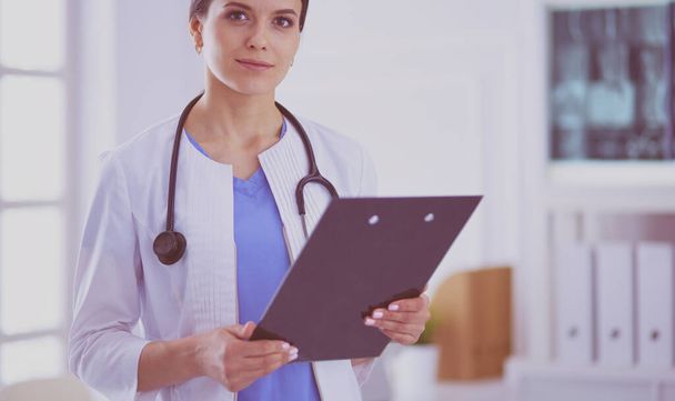 Young smiling female doctor with stethoscope holding a folder at doctors office - Фото, изображение
