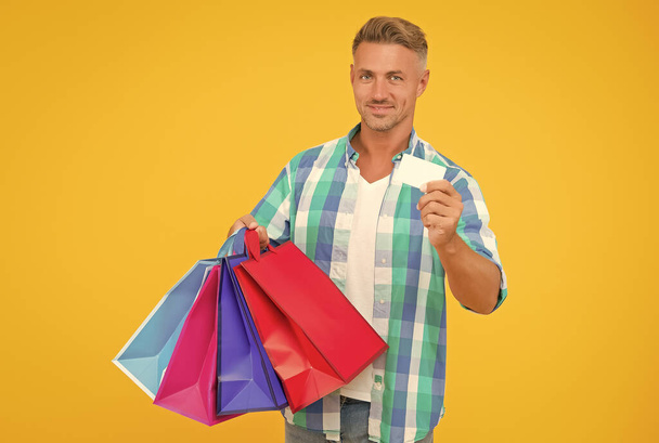 happy handsome man holding packages with purchase preparing for holiday and show credit card, new year greeting - Photo, Image