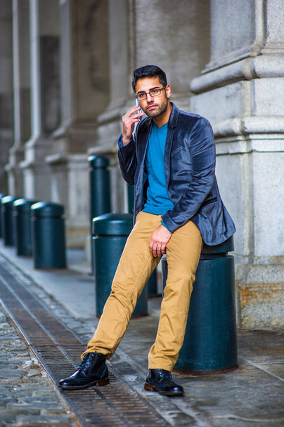 Одеваясь в голубой шерстяной пиджак, свитер, темно-желтые брюки и кожаные ботинки, в очках, молодой парень с хлебом и усами сидит на улице старой моды, делает телефонный звонок - Фото, изображение