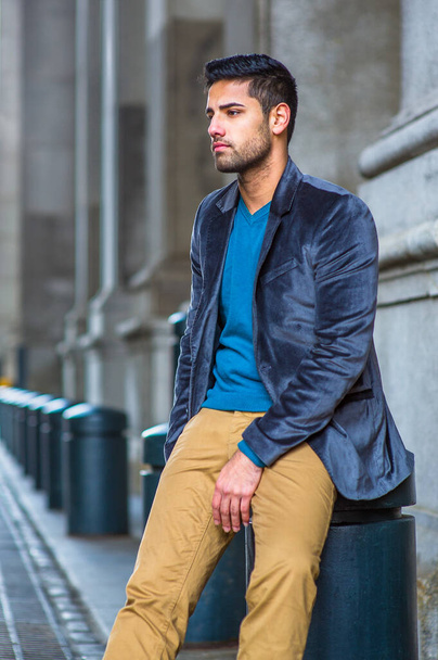 In blauem Wollblazer, Pullover und dunkelgelber Hose sitzt ein junger Mann mit Brot und Schnurrbart auf einer Straße der alten Mode und denkt tief darüber nach. - Foto, Bild