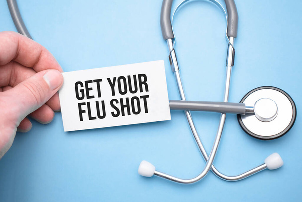 the doctor's hands holds a business card with the text of Get Your Flu Shot with one hand and the other points to the text. - Foto, imagen