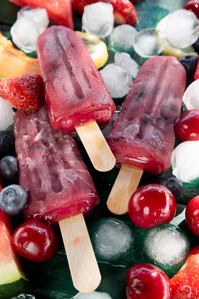 Photographic shot of popsicles made with red fruit on a table served with various fruit  - Foto, imagen