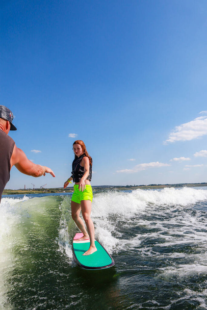 El entrenador le enseña a la chica a levantarse en el wakesurf. Barco y entrenamiento. Lago.. - Foto, Imagen