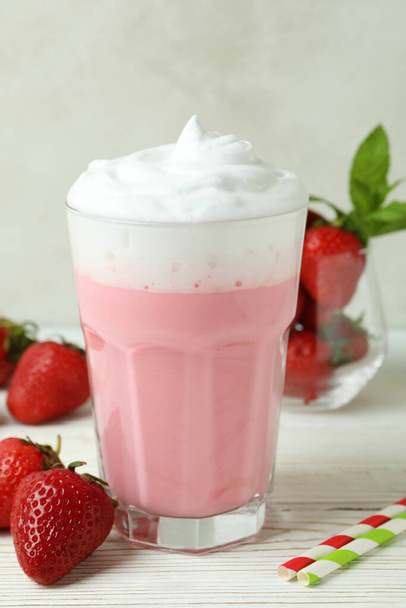 Glass of strawberry milkshake and ingredients on white wooden table - Photo, Image