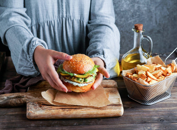Vegane Linsenburger in Frauenhand, mit Salat und Joghurtsoße auf weißem Hintergrund. Pflanzliches Ernährungskonzept. - Foto, Bild