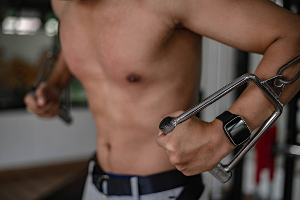 Fitnessstudio-Konzept eines muskulösen männlichen Teenagers mit einem Fitnessgerät, das sich wiederholt, um seine Brust zu entwickeln. - Foto, Bild
