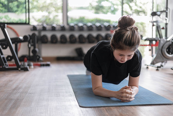Concepto de gimnasio de entrenamiento una adolescente haciendo tablado y manteniendo la posición durante un tiempo como su ejercicio abdominal y central. - Foto, Imagen