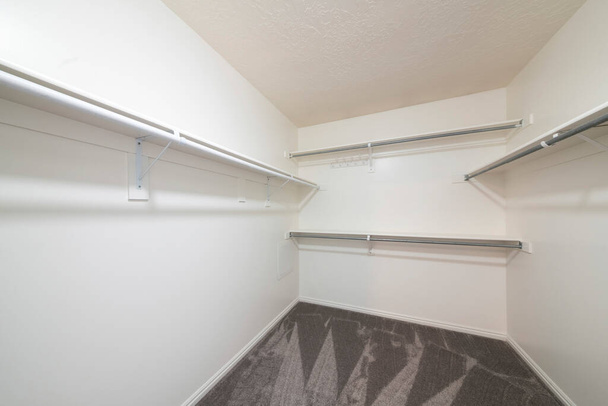 White empty walk in closet with carpeted floor and shelves with metal hanging rods - Photo, Image