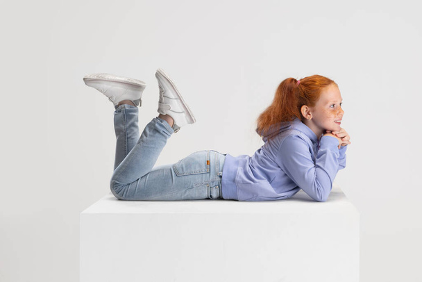 Side view. Portrait of smiling red-headed girl in casual clothes isolated on white studio background. Happy childhood concept. Sunny child. Looks happy, delighted - Fotografie, Obrázek