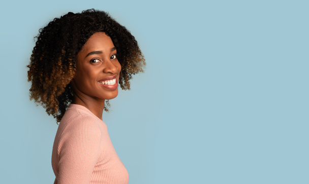 Szczęśliwa czarna kobieta. Uśmiechnięta młoda Afroamerykanka pozowanie na niebieskim tle - Zdjęcie, obraz