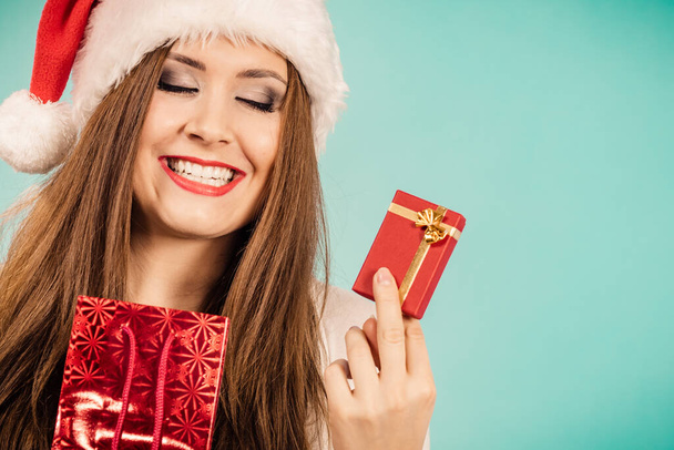 Christmas gifts. Happy woman wearing santa claus hat holding present red bag and small gift box with jewelery, on blue - Foto, afbeelding
