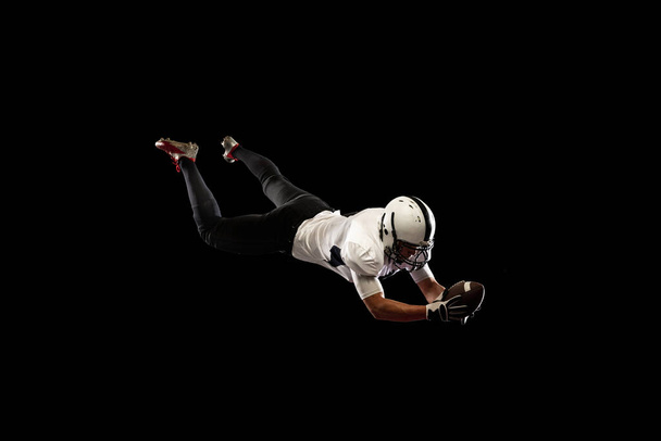 Portrait young American football player, athlete in black white sports uniform training isolated on dark studio background. Concept of professional sport, championship, competition. - Foto, immagini