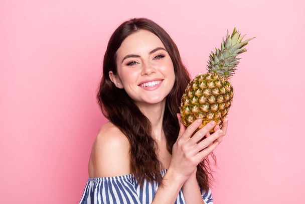 Photo of shiny adorable young lady wear off-shoulders clothes smiling holding pineapple isolated pink color background - Фото, изображение