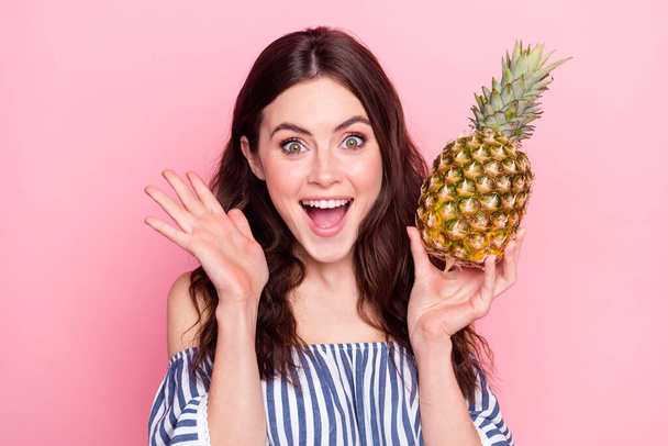 Photo of cute impressed young woman dressed striped outfit rising arms holding fruit isolated pink color background - Zdjęcie, obraz
