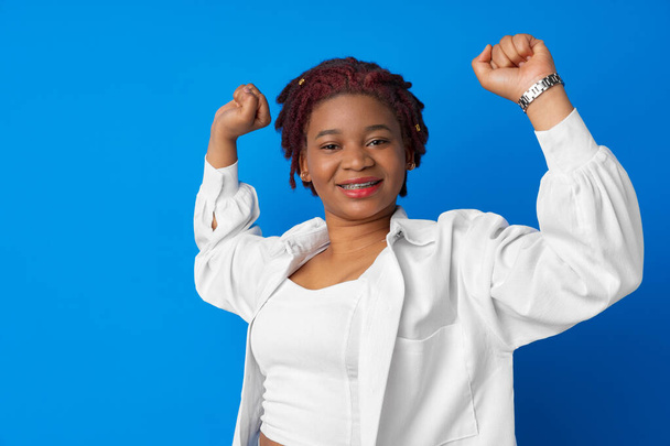 Portrait of a cheerful young african woman with hands raised against blue background - Foto, immagini